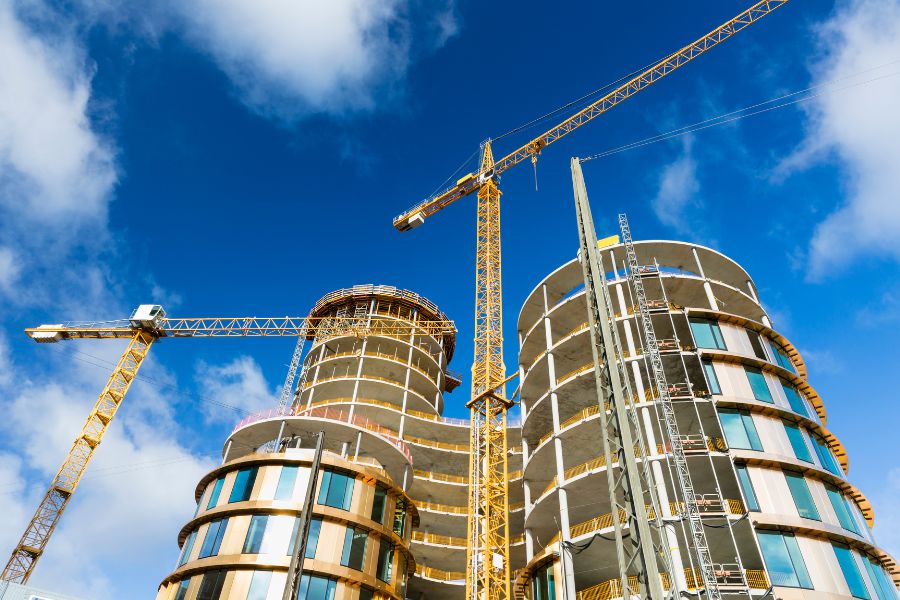 A construction crane positioning a structural steel beam onto the skeleton of a new high-rise building in Montreal, supplied by Acier Lachine.