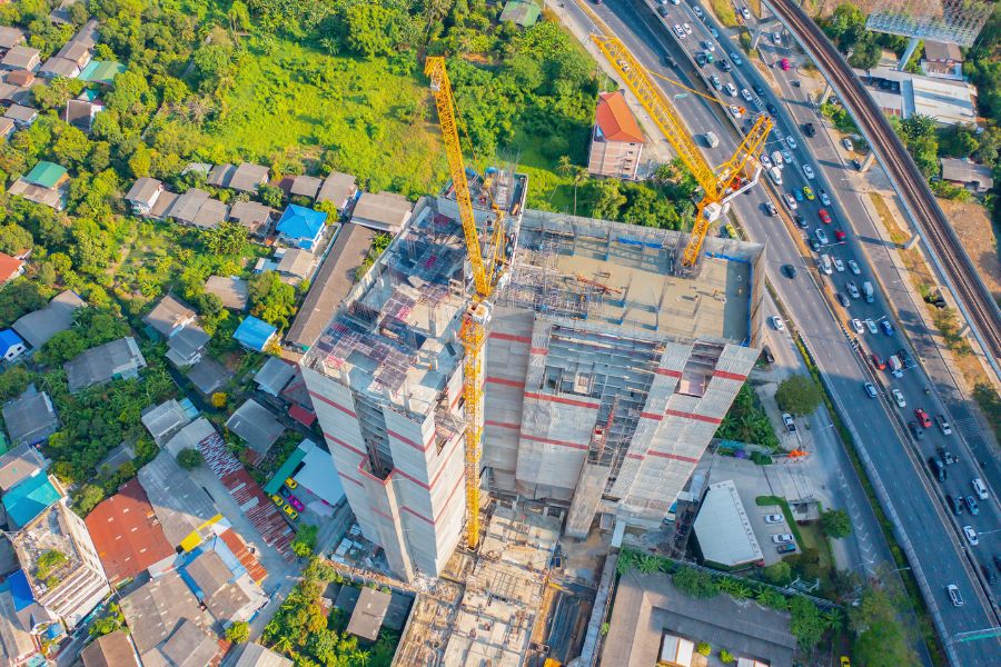 Active multi-trade construction site using a tower crane to install complex structural steel and reinforcing bars (rebar). Building 01.