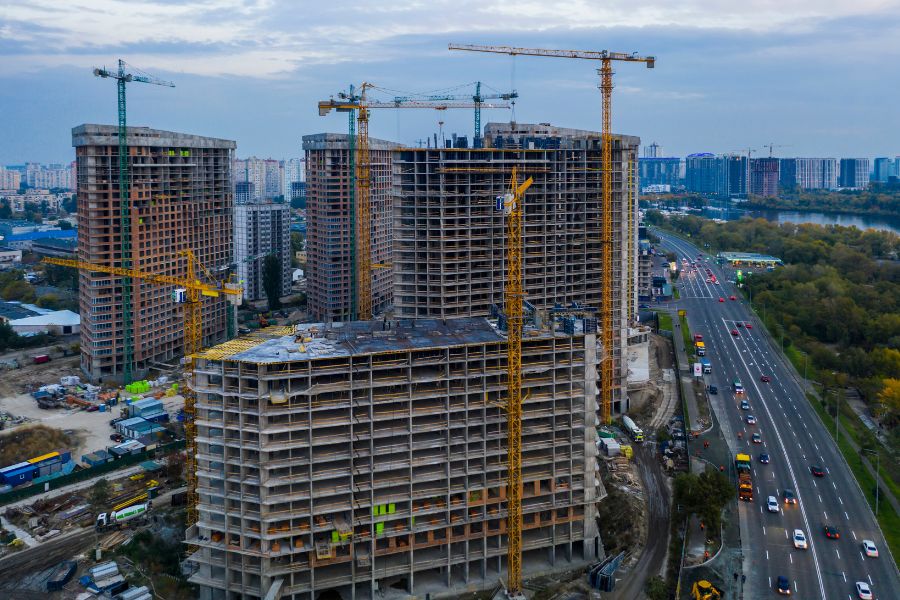 Active multi-trade construction site using a tower crane to install complex structural steel and reinforcing bars (rebar). Building 02.
